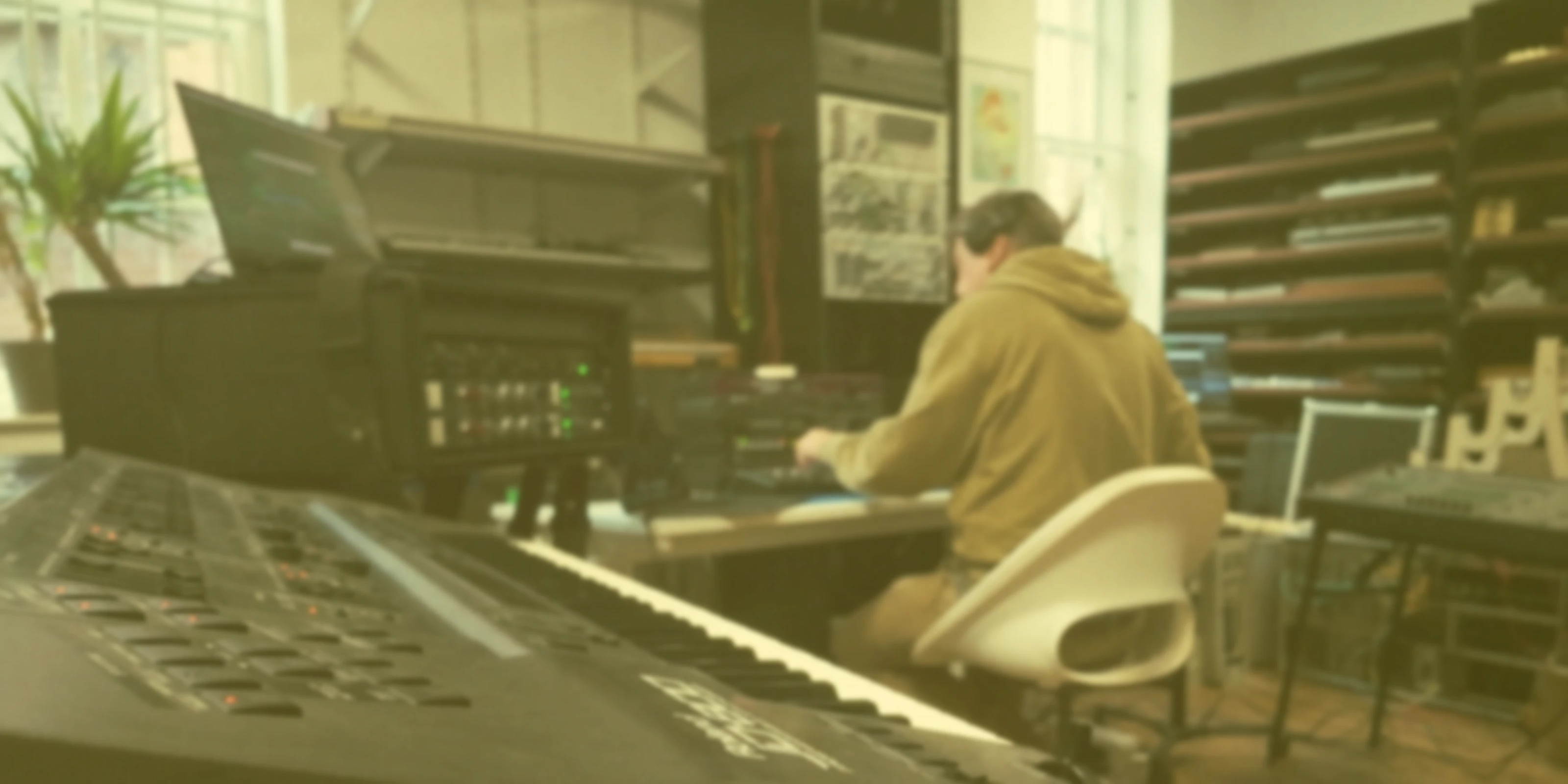 Person working at a music production station with electronic instruments and computers.
